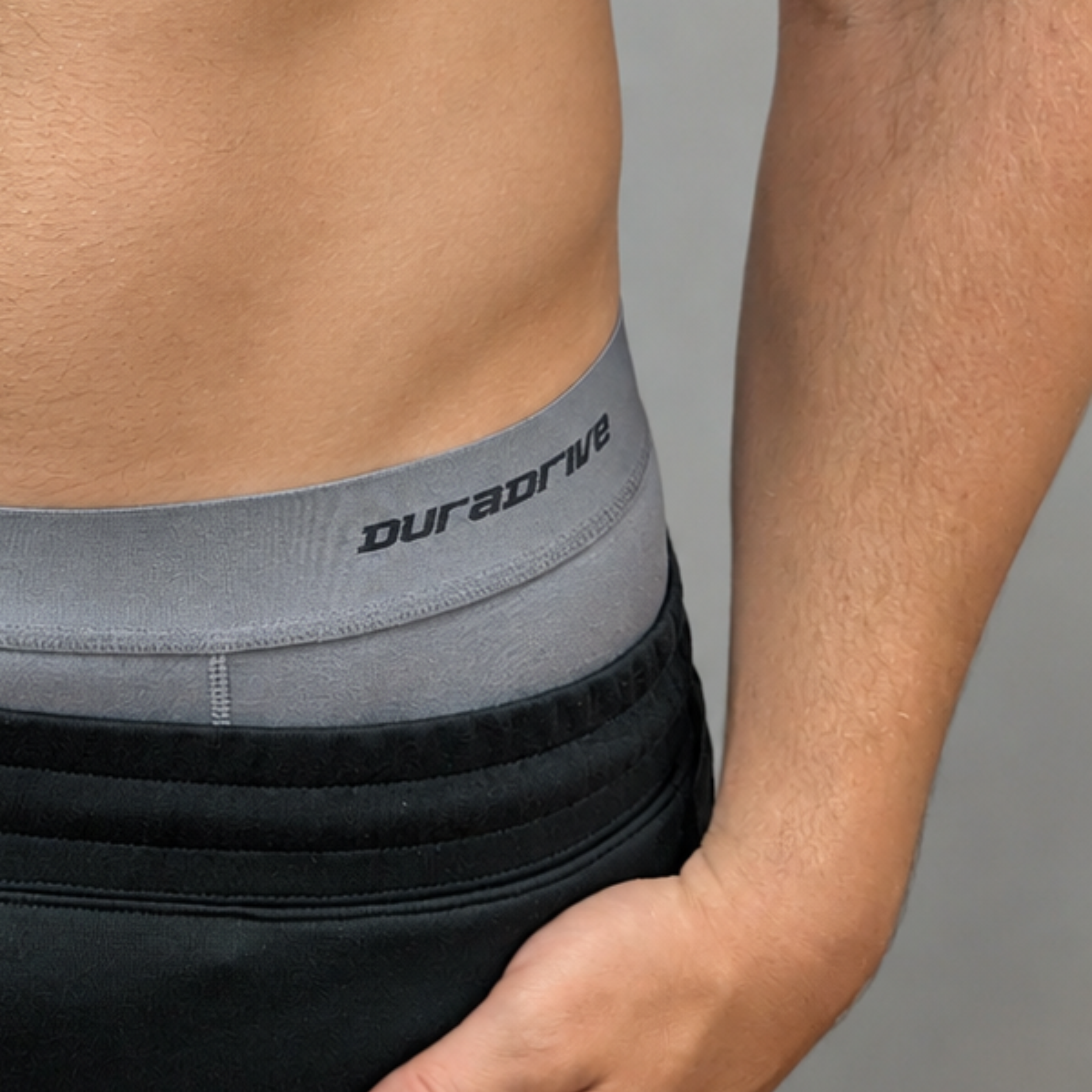 Close-up of a person wearing black athletic shorts with a gray waistband featuring the brand name 'duradrive' in black text.